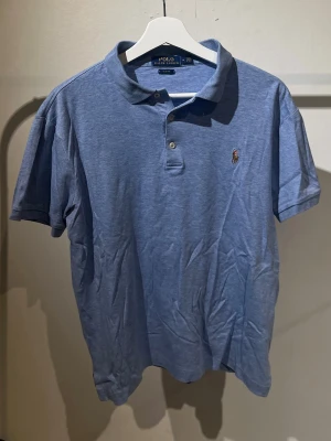  Piké Tröja från Ralph Lauren - Klassisk blå pikétröja från Polo Ralph Lauren med broderad logga på bröstet. Tröjan har korta ärmar, krage och knappar framtill. Slim fit-modell i mjuk bomull som passar perfekt till jeans eller shorts. Storlek M men passar S.