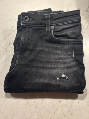 Svarta slitna jack and Jones jeans - Säljer ett par svarta Jack and Jones jeans med slitningar och tvättade detaljer. Jeansen har skön passform. Perfekta för en avslappnad och trendig look. Hör av er vid funderingar🙌