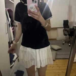 Vit volangkjol med broderade detaljer - Supersöt vit kortkjol med flera lager volanger och broderade detaljer. Kjolen har resår i midjan för en bekväm passform och är perfekt att styla med en enkel t-shirt eller crop top. Lätt och luftig känsla, perfekt för varmare dagar.