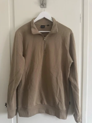 Beige halfzip från Only & Sons - Snygg beige halfzip-tröja från Only & Sons med hög krage och dragkedja framtill. Tillverkad i mjukt bomullsmaterial och har långa ärmar samt ribbade muddar. Sparsamt använd.