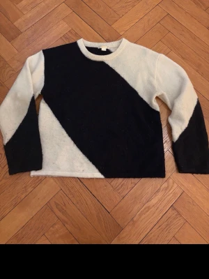 Gina svartvit tröja  - Säljer en stickad tröja i svart och vitt med cool diagonal färgblock-design. Tröjan har rund halsringning och långa ärmar. Materialet ser mjukt och mysigt ut, perfekt för kyligare dagar. Passar dig som gillar grafiska mönster och enkel stil.