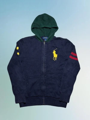 Vintage Ralph Lauren grovstickad hoodie - herr strl L, passar som S - Säljer en vintage Ralph Lauren marinblå grovstickad hoodie med mörkgrön luva i storlek L, passar som S. Stor broderad Ralph Lauren hästlogga samt “3” broderat på höger ärm och två röda sträck på vänster ärm.  👕 Märke: Ralph Lauren 📏 Storlek: L, passar som S 🎨 Färg: Marinblå med grön luva 🧵 Material: 100% bomull 📐 Mått: 64 cm lång, 49 cm bred 📌 Skick: Mycket bra skick, storleksetikett borta (se bilder)  💬 Hör av dig vid frågor 💰 Pris kan diskuteras vid snabb affär 📦 Skickas inom 24 timmar