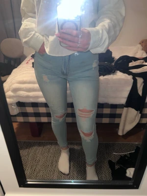 Ljusblå ripped skinny jeans från Shein - Säljer ett par ljusblå skinny jeans med slitningar och hål på både lår och knän. Jeansen har hög midja och klassisk femficksdesign. Perfekta för en avslappnad och trendig look.