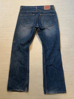 Levi's 507 bootcut - Klassiska blå jeans från Levi's med bootcut passform och fem fickor. Jeansen har en snygg tvättad look och detaljer som kopparfärgade nitar och läderpatch bak i midjan. Tillverkade i slitstark denim, perfekta för en avslappnad stil.