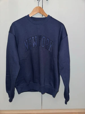 Mörkblå sweatshirt New York Junkyard - Mörkblå sweatshirt från Junkyard med broderad text 'NEW YORK' på bröstet. Helt ny med prislappen kvar säljer pga fel storlek. Strl xs kan diskutera pris. Ordinarie pris var 600.