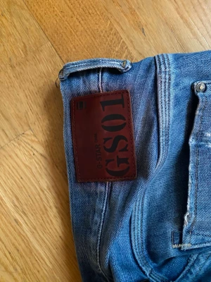 Blå G-Star RAW jeans herr - Säljer ett par klassiska blå jeans från G-Star RAW med snyggt slitna detaljer och rak passform. Jeansen har fem fickor, läderpatch med logga bak och är tillverkade i slitstark denim. Perfekta för en avslappnad och trendig look.