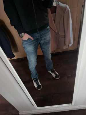 Blå jeans snygg tvätt  - Säljer ett par blå jeans från Frankrike med klassisk femficksmodell och snygga slitningar. Jeansen har snygg passform samt en patch med logga bak i midjan. Perfekta till sneakers och hoodie för en avslappnad look.
