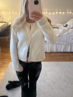 GINA TRICOT - kofta  - Mysig vit kofta med fluffig känsla och rund halsringning. Koftan har långa ärmar och stängs med små vita knappar framtill. Passar perfekt till jeans eller kjol för en enkel och stilren look.