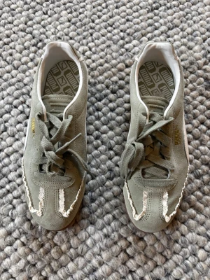 Gröna sneakers från Puma - Snygga gröna sneakers från Puma i mocka med vita detaljer och guldfärgad logga på sidan. Skorna har låga skaft, vita sicksack-sömmar framtill och klassisk snörning. Perfekta för en avslappnad och trendig stil.