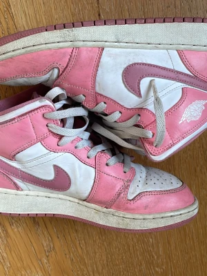Nike Air Jordan 1 Mid rosa/vit - Säljer ett par Nike Air Jordan 1 Mid sneakers i rosa och vitt läder med klassisk Swoosh och Air Jordan-logga på sidan. Skorna har vita skosnören och en rosa yttersula. Perfekta för dig som vill sticka ut med en ikonisk och färgglad sneaker. Jätte fin sko och har andvänt mycke men ändå i helt okej skick. Kommer även tvättas och byta skosnören innan köp 