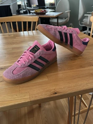 Adidas gazelle - Säljer ett par rosa Adidas sneakers  med klassiska svarta stripes på sidorna och gummisula. Skorna har lågt skaft och detaljer i mörkblått vid hälen. Perfekta för dig som vill sticka ut med färg och stil. Använda ett fåtal gånger och är i väldigt bra skick!