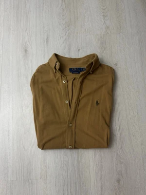 Brun overshirt/skjorta från Polo Ralph Lauren - Snygg brun overshirt från Polo Ralph Lauren med klassisk krage och knäppning framtill. Långärmad modell med broderad logga på bröstet. Tillverkad i mjukt tyg som ger en avslappnad men stilren look.