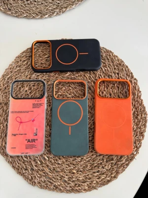 Färgglada MagSafe-kompatibla mobilskal - Fyra snygga mobilskal för iPhone 17 PRO Max med MagSafe-stöd. Skalen är i färgerna svart, orange, grön och ett transparent med grafiskt tryck. De har markerad MagSafe-ring och stora kamerauttag. Perfekt för dig som vill sticka ut med din mobil!