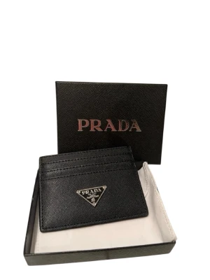 Svart kortfodral från Prada - Snyggt svart kortfodral från Prada i äkta läder med elegant struktur. Fodralet har flera kortfack och pryds av Pradas ikoniska metallogo framtill. Perfekt för dig som vill ha en stilren och lyxig accessoar i fickan.