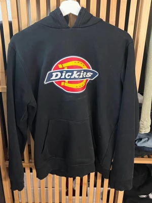 Svart Dickies hoodie med logga - Svart hoodie från Dickies med stor färgglad logga på bröstet. Klassisk känguruficka framtill och huva. Tillverkad i mjukt material som passar perfekt för en avslappnad streetwear-look.