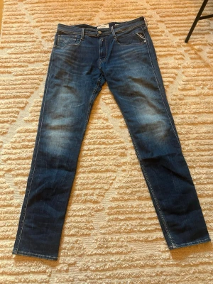 M polotighta blå jeans från Replay - Säljer ett par snygga blå jeans från Replay med klassisk femficksmodell och diskreta slitningar framtill. Jeansen har reasoned sopade detaljer och raka ben sopade detaljer. Materialet är mjukt denim med vita sö stronga kontrastsömmar. Helt oanvända.