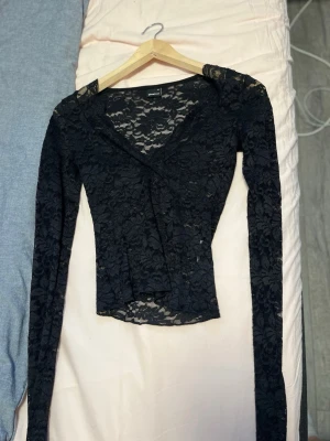 Svart spetsblus med v-ringning - Snygg svart blus i genombruten spets med v-ringad hals och långa ärmar. 
