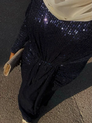 Mörkblå glittrig långklänning - Säljer en elegant mörkblå långklänning täckt av glittrande paljetter. Klänningen har lång ärm och markerad midja för en snygg siluett. Perfekt för dig som vill sticka ut med en lyxig look.