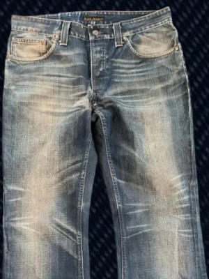 Nudie jeans Bootcut Ola 34 32 - Ett par riktigt snygga Nudie Jeans Bootcut Ola! Storlek på taggen: 34/32 (Se mått nedan). Fint skick, har slitningar och patina från användning, t.ex två mindre hål i båda bakfickor. Skriv om du har frågor! Mått: Storlek på tag - 34/32, Midja - 43 cm, Lår - 28 cm, Innersöm - 80 cm, Längd - 105 cm, Benöppning - 23.5 cm