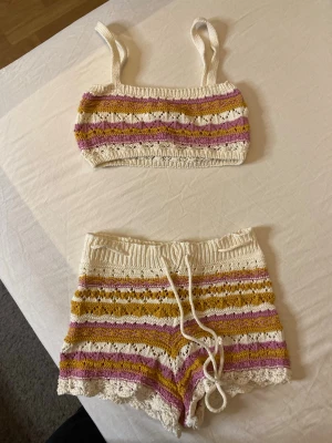 Stickat set med topp och shorts - Säljer ett stickat set med topp och shorts i vitt, lila och senapsgult. Perfekt för en avslappnad och trendig look.