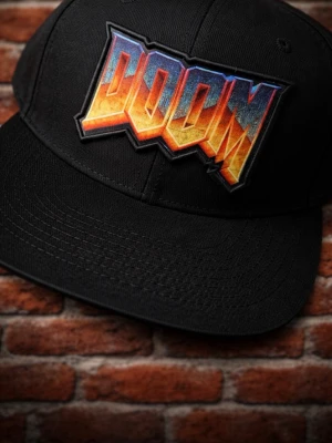 Svart DOOM snapback keps - Säljer en svart snapback keps med stort broderat DOOM-logotyp i rött, orange,blå  och gult framtill. Kepsen har platt skärm och justerbar plastrem bak för perfekt passform. Materialet är tåligt och passar dig som gillar gaming och streetwear.