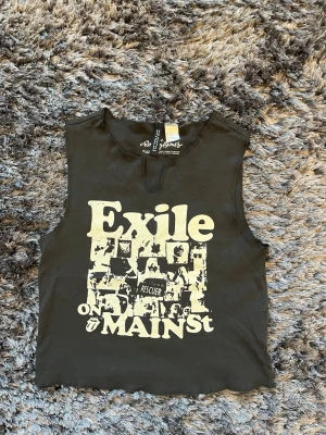 Svart croppad linnetopp Exile - Cool svart croppad linnetopp från H&M DIVIDED, Recycled Karma med tryck 'Exile on Main St' och grafiskt motiv framtill. Toppen är ärmlös och har råa kanter samt en liten slits vid halsen. Perfekt för en edgy och avslappnad stil. Aldrig använt då den är för liten. Strlk XXS. ALLA PRISER IAN DISKUTERAS🤍