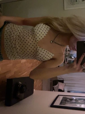 Prickig vit linnetopp med v-ringning - Snygg vit linnetopp med svarta prickar och v-ringning. Toppen är ärmlös och har en figurnära passform som framhäver siluetten. Perfekt att styla med jeans eller kjol för en trendig look.