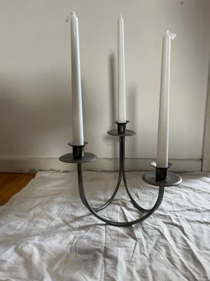 Stilren metall ljusstake för tre ljus - Säljer en snygg och modern ljusstake i metall med plats för tre smala stearinljus. Ljusstaken har en rund, böjd design och är i en matt silverfärg. Perfekt som dekoration på matbordet eller i vardagsrummet.