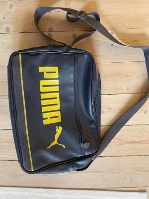 Blå och gul axelväska från Puma - Snygg blå axelväska från Puma med gul logga och text på framsidan.