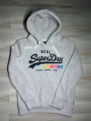 Ljusgrå hoodie från Superdry - Säljer en ljusgrå hoodie från Superdry med stor logga och japansk text framtill🤩 fint skick små defekter som inte syns vid användning😇 Hör av er vid snabbaffär samt funderingar🙌🏻