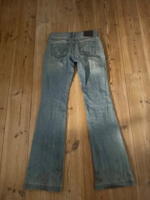 Ljusblå bootcut jeans - Säljer ett par ljusblå bootcut jeans med klassisk femficksdesign och slitna detaljer. Jeansen har en något utsvängd passform nedtill och är tillverkade i denim. Perfekta för dig som gillar en avslappnad och retro stil.