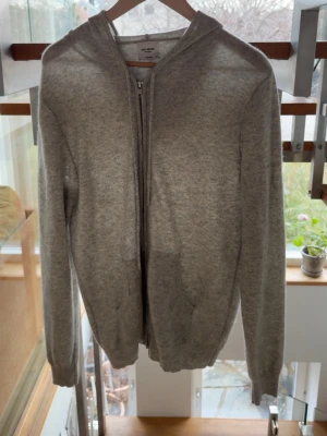 John Henric Kashmir zip up hoodie  - En enkel och stilren grå hoodie från John Henric med dragkedja framtill och huva. Tillverkad i 100% Kashmir och har långa ärmar samt ribbade muddar vid ärmslut och nederkant. Perfekt för en avslappnad look. Använd fåtal gånger. 