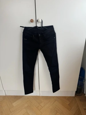 Svarta skinny jeans från Tiger of Sweden  - Säljer ett par svarta skinny jeans från Tiger of Sweden. Jeansen har fem fickor, smal passform och klassisk knappgylf. Materialet är stretchigt för extra komfort och de har diskreta detaljer vid fickorna. Perfekta för en clean och stilren look.