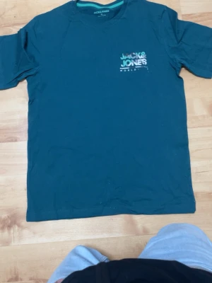 Blå Jack & Jones t-shirt - Snygg blå t-shirt från Jack & Jones med tryck på bröstet. Klassisk rund hals och korta ärmar. happening-vibe och passar perfekt till jeans eller shorts. Tillverkad i mjuk bomull för skön känsla hela dagen.