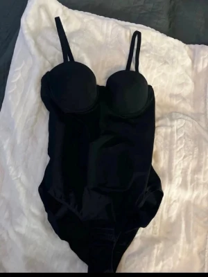 Svart push up body  - Snygg svart body med bygelkupor och justerbara axelband. Bodyn har en slät, stretchig yta och knäppning i grenen för enkel på- och avtagning. Perfekt för att skapa en stilren och självsäker look.