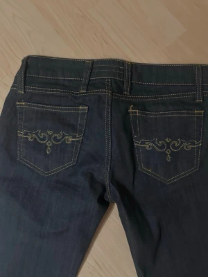 Mörkblå jeans med broderade fickor - Säljer ett par vintage mörkblå bootcut jeans med snygga guldfärgade broderier på bakfick. Kommer sitta bra på en lång tjej (jag är 172cm och dem sitter perfekt)
