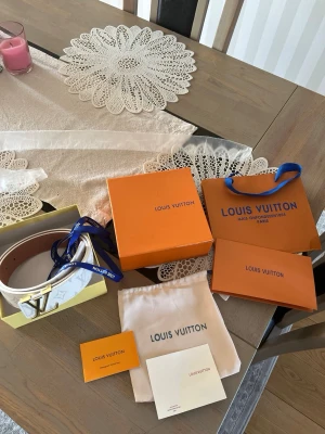 Vitt monogram bälte från Louis Vuitton - Snyggt vitt bälte från Louis Vuitton med Bred design och ikoniskt LV-spänne i guld. Bält sopackas med originalbox, dustbag och certifikat. sopassande till jeans eller klänning för en lyxig touch har varit använd tre gånger och ett eget hål med lite slitnad o är 99% säker på att den är äkta svarar på frågor o kan skicka mer bilder på sakerna
