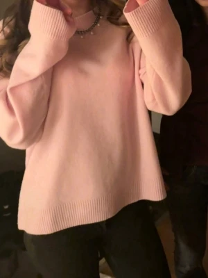 Ljusrosa oversized stickad tröja - Mysig ljusrosa stickad tröja med oversized passform och långa ärmar. Tröjan har ribbade muddar vid ärmslut och nederkant. 