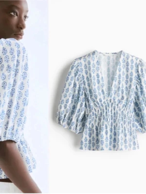 Vit blus med blått mönster och puffärm - Säljer en vit blus med blått paisleymönster och djup v-ringning. Blusen har puffiga, trekvartsärmar och smockad midja som ger en snygg siluett. Materialet är lätt och luftigt, perfekt för sommarens outfits.