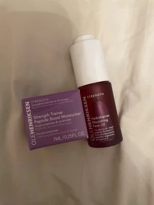 OLEHENRIKSEN Strength ansiktsolja & kräm - Säljer OLEHENRIKSEN Strength Trainer Peptide Boost Moisturizer och HydraBarrier Nourishing Face Oil. Krämen kommer i en lila förpackning och oljan i en röd flaska med vit pump. Båda innehåller peptider, ceramider och vitamin E, perfekt för att stärka och återfukta huden.