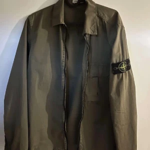 Grön overshirt från Stone Island - Original pris 3600 kr!  Snygg olivgrön overshirt från Stone Island med klassisk patch på ärmen. Overshirten har rak passform, bröstficka och är tillverkad i bomull. 