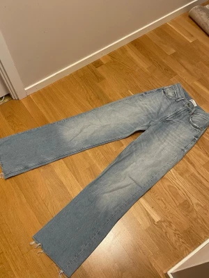 Ljusblå wide jeans från Zara - Säljer ett par ljusblå raka jeans från Zara med råa, fransiga benslut och klassisk femficksmodell. Jeansen har hög midja och är tillverkade i bomull för en skön och avslappnad look. Perfekta till sneakers eller boots.