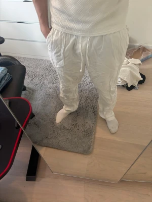 Vita linnebyxor med dragsko - Säljer ett par vita linnebyxor med avslappnad passform och dragsko i midjan. Byxorna har raka ben och sidofickor, perfekta för en chill och stilren look. Materialet är lätt och luftigt, vilket gör dem sköna att bära under varma dagar.