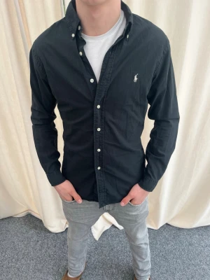 Svart skjorta från Ralph Lauren - Riktigt snygg skjort från Ralph Lauren. Strl S, personen på bilden är 184 cm lång.Inga defekter. Skicka gärna prisförslag. Kika in min profil för mer schyssta plagg