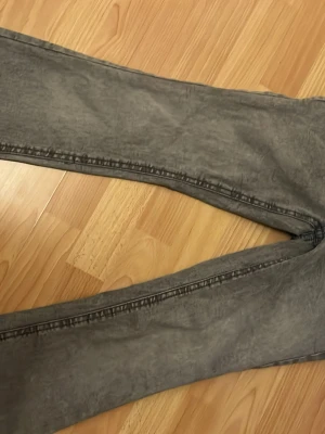 Grå tvättade jeans med fickdetaljer - Säljer ett par grå tvättade jeans med raka ben och stora bakfickor med lock och knapp. Jeansen har en avslappnad passform och cool vintagekänsla. Perfekta för dig som gillar en streetwear-look.