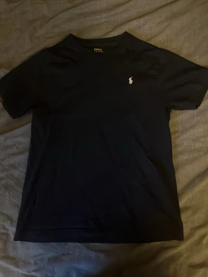 Svart t-shirt från Polo Ralph Lauren - Snygg svart t-shirt från Polo Ralph Lauren med klassisk passform och den ikoniska vita logon broderad på bröstet. Tillverkad i mjuk bomull och har korta ärmar. Perfekt basplagg för en clean och stilren look.