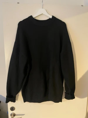 Svart oversized stickad tröja Jack and Jones XL - En svart, oversized stickad tröja med rund halsringning och ribbade muddar vid ärmslut och nederkant. Perfekt för lager på lager och en clean look. Materialet ser ut att vara mjukt och tjockt, vilket gör den extra mysig under kyliga dagar.