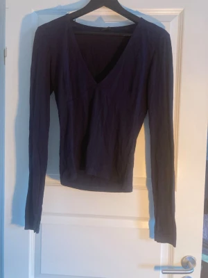 Mörkblå långärmad v-ringad topp - En stilren mörkblå långärmad topp med v-ringning. Toppen har en figurnära passform och är tillverkad i ett mjukt bomullsmaterial. Perfekt att matcha med jeans eller kjol för en enkel och snygg look.