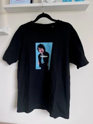 Håkan Hellström-t-shirt, svart/blå, S (unisex) - Svart Håkan Hellström-t-shirt med blått tryck ”Håkan” på framsidan. Unisex S.  💎 Knappt använd, mycket bra skick (säljs ej längre) 📏 Bröstvidd/längd: 51/66 cm 💰 399 kr