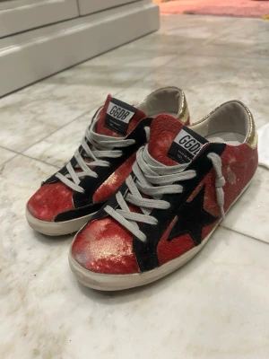Golden Goose röda och guld sneakers - Unika sneakers från Golden Goose i rött och guld köpta på butiken i Rom. De är i super bra skick som man ser på sulorna, slitningarna är en del av designen. 